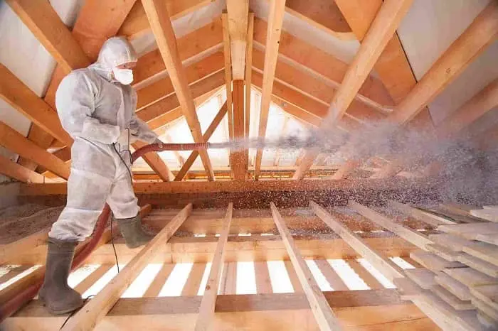 Two Home Insulation Installers working on insulating a house. One is holding a hose to spray insulation foam into the walls while the other is using a tool to spread it evenly.
