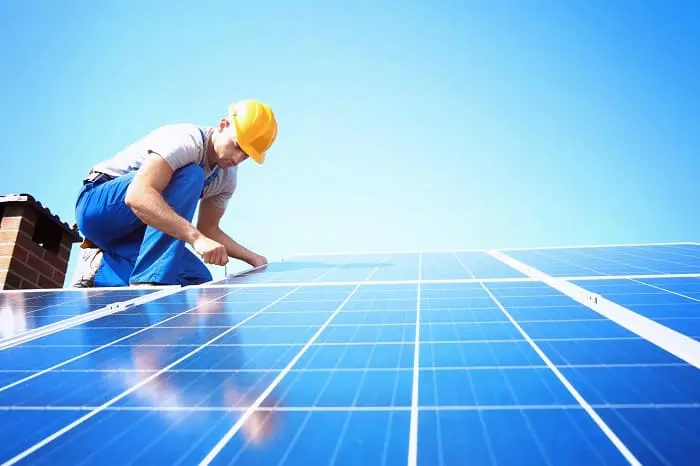 A Solar Installation technician is sitting on a roof installing solar panels.